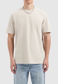 Beige katoenen t-shirt met korte mouwen en een ronde hals, met een subtiele logo-detaillering aan de onderzijde en een ontspannen pasvorm.