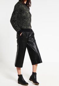 Sweter dziany w czarno-zielony wzór, zestawiony z czarnymi skórzanymi kulotami i botkami za kostkę, ozdobionymi złotymi detalami.