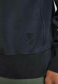 Sweatshirt marine à ourlet et poignets côtelés, tissu texturé, avec un logo « PULL » embossé sur le côté inférieur. Conception à coupe décontractée.