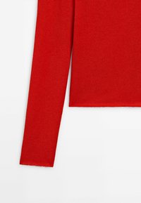 T-shirt long à manches rouges en tricot avec un col rond, texture lisse et ourlet droit, dotée de poignets côtelés aux manches.