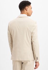 Beige colbert gemaakt van lichtgewicht stof, met een enkele split, gekartelde revers en knopen met drie knopen aan de mouwen. Glad structuur.