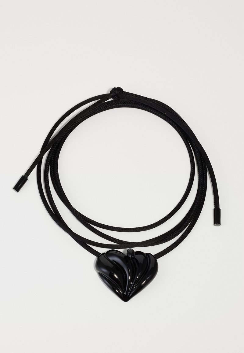Ciondolo a forma di cuore nero su un elegante cordino nero. Il ciondolo presenta un design lucido e testurizzato con righe in rilievo e una finitura liscia.