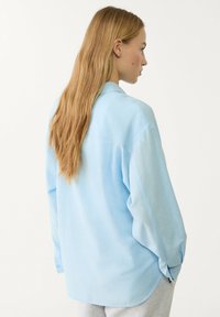 Light blue oversized shirt with a collar, long sleeves, and button cuffs. Soft fabric with a smooth texture and a relaxed fit.