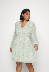 Vestido floral verde claro com mangas longas bufantes, decote em V e cintura atada. Feito de um tecido leve, apresentando pequenos padrões florais brancos e verdes.