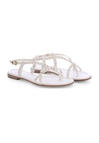 Weiße flache Sandalen mit mehreren Riemen, die mit runden Nieten verziert sind, ausgestattet mit einem verstellbaren Knöchelriemen und einer strukturierten Sohle.
