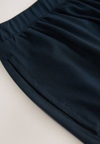 Gros plan sur un pantalon bleu foncé avec une taille élastique et une poche latérale avec des coutures visibles.