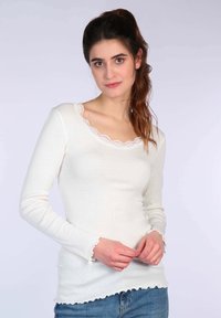 Weißes Langarmshirt mit geripptem Stoff, verziert mit einem gewellten Spitzenkragen und Bündchen. Kombiniert mit Jeans.