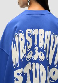 Sudadera azul con texto estilizado en blanco y grande en la parte posterior. Cuello de trip only y tejido suave con un corte relajado.