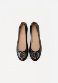 Ballerines en cuir noir avec bouts ronds, ornées de grands accents métalliques au logo à l'avant. L'intérieur est beige et présente une texture lisse.