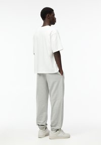 Witte katoenen oversized t-shirt gecombineerd met lichtgrijze sweatpants. De broek heeft boorden bij de enkels en zijzakken. Witte sneakers worden gedragen.
