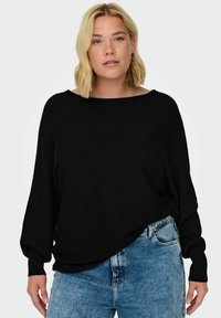 Black ribbed long-sleeve top with a wide neckline, loose fit, and soft texture. Paired with faded blue high-waisted jeans.