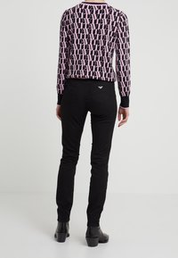 Långärmad tröja med ett rosa och svart upprepande logotypmönster och ribbad halsringning. Svarta figursydda byxor med en liten emblema på baksidan.