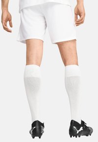 Weiße Sportshorts und kniehohe weiße Socken kombiniert mit schwarzen Fußballschuhen mit strukturiertem Design und Logodetail.