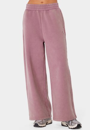 Luźne, fioletowe spodnie dresowe z elastycznym pasem noszone z srebrnymi i szarymi butami do biegania.