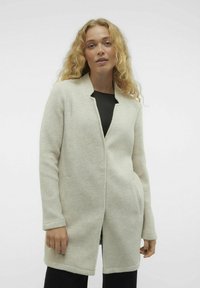 Cappotto grigio chiaro realizzato in un materiale morbido, con colletto a risvolto, tasche nascoste e una linea dritta che arriva sotto i fianchi.