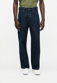 Σκούρο μπλε τζιν με άνετη εφαρμογή, που διαθέτει πέντε τσέπες, κούμπωμα με κουμπιά και αντίθετη ραφή κατά μήκος των πλευρικών ραφών.