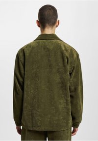Green corduroy jacket with a textured finish, featuring a soft collar, loose fit, and visible ribbed pattern. Back view shown.