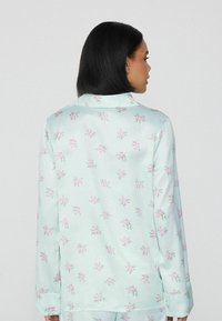 Helles blaues Schlafanzug-Oberteil mit einem floralen Muster in Pink, mit Kragen und langen Ärmeln, aus glattem Stoff gefertigt. Das Design ist in lockerer Passform.
