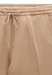 Beige cotton joggers with an elastic waistband and drawstring, featuring front pleats and a smooth texture.