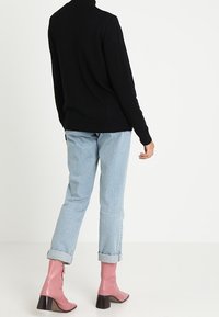Zwarte coltrui, lichtblauwe opgerolde jeans en glanzende roze enkellaarsjes met een vierkante hak, gezien vanaf de achterkant.