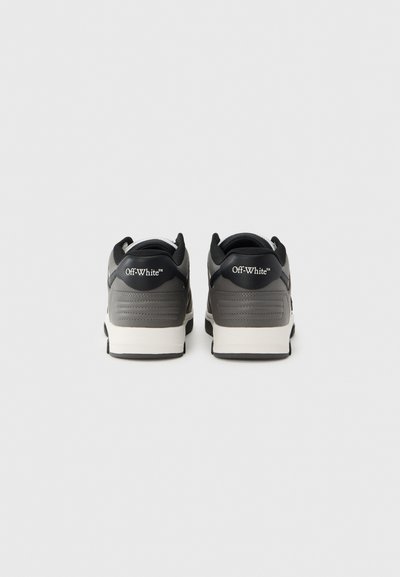 Μαύρα και γκρι αθλητικά παπούτσια με λείο δερμάτινο επάνω μέρος, στρογγυλεμένη μύτη και λευκή φέρουσα σήμανση στο πίσω μέρος. Υφασμένοι τόνοι στη φτέρνα και στις πλευρές.