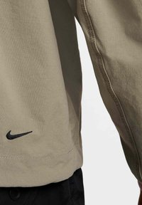 Långärmad skjorta i ljus khakifärg, med en svart Nike-logotyp vid fållen och kontrasterande sömnadsdetaljer längs sömmarna.