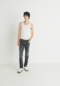White tank top, dark denim jeans, and white sneakers. The jeans have a classic fit, and the tank top is lightweight. Simple, unadorned textures.