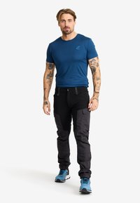 Blå kortärmad t-shirt, svarta cargo byxor med sidofickor, och blå träningsskor, visade mot en enkel vit bakgrund.