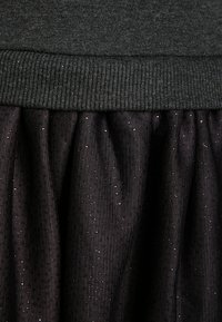 Schwarze Rock mit einem schwarzen Strickbund, der einen strukturierten, gerafften unteren Teil mit glitzernden Details aufweist. Der Stoff ist weich und dehnbar.