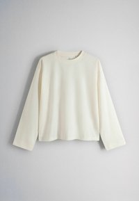 Long-sleeve, plain cream-colored crewneck shirt displayed against a light gray background.