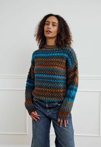 Kootud kampsun, millel on mitmevärviline muster pruunidest, türkiissinistest ja sinistest triipudest. Ümar kaelus ja pikad varrukad soonikkoes mansettidega. Sobitatud siniste teksadega.