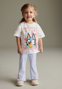 Fehér pamut póló színes, rajzfilmszerű kutyaábrázolással, világoskék bordázott, bővülő szárú nadrággal, rózsaszín virágmintákkal.