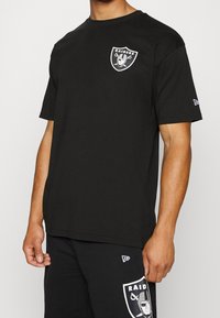 Svart bomulls t-shirt med en vit Raiders-logotyp på bröstet. Korta ärmar och design med rund halsringning. Mjuk textur.