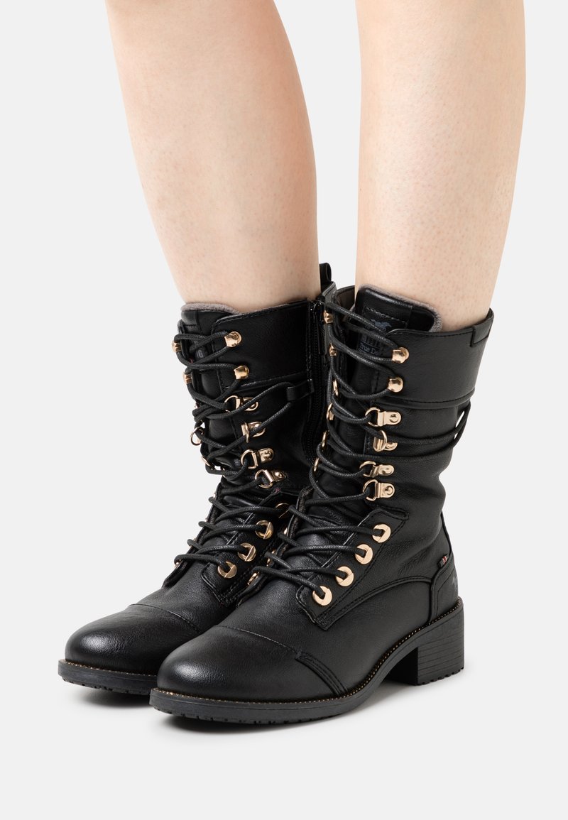 Bottes montantes en cuir noir à lacets avec œillets dorés, une pointe arrondie et un petit talon carré. Équipées d'une fermeture éclair sur le côté pour un enfilage facile.