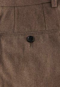Pantalones de tela marrón con un acabado texturizado, con un botón negro y detalles de bolsillo ajustados. Diseño clásico con un material suave.
