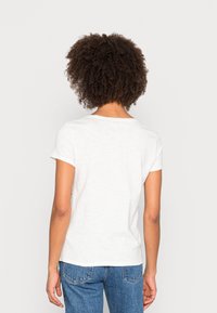 T-shirt bianco in cotone con maniche corte, colletto rotondo e vestibilità rilassata, abbinato a jeans di denim blu. Texture sottile e design classico.