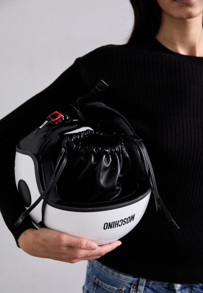 Hvid hjelm med sort indre og snørretaske, med en rød låsemekanisme. Håndholdt, med et enkelt, strømlinet design og synlig branding.
