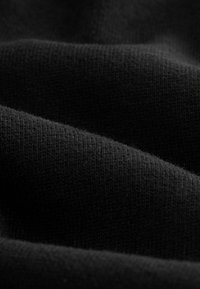 Schwarzer Strickstoff mit einer weichen Textur, der subtile Variationen in der Webart aufweist und ein glattes, fließendes Erscheinungsbild in geschichteten Falten schafft.