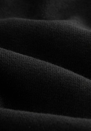 Tessuto knit nero con una consistenza morbida, caratterizzato da sottili variazioni nella tessitura, creando un aspetto fluido e liscio in pieghe stratificate.