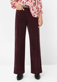 Pantalon large en velours côtelé de couleur bordeaux profond, avec poches avant et texture lisse, associé à un chemisier rose à motifs.