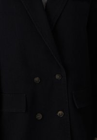 Blazer croisé bleu marine foncé en tissu lisse, doté de deux grandes poches, six boutons ronds et d'un col classique.