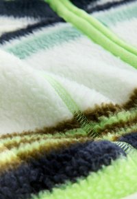 Tissu en polaire douce avec des rayures horizontales vertes, blanches, marron et bleu marine, avec un détail de couture verte visible.