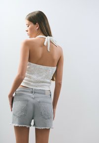 Top de encaje blanco tipo halter con lazo en la espalda, combinado con shorts de mezclilla gris claro que presentan adornos en forma de estrella en los bolsillos y dobladillos deshilachados.