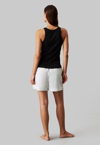 Canotta nera abbinata a pantaloni corti bianchi fino al ginocchio. La canotta presenta un design aderente, mentre i pantaloni corti hanno una texture liscia e spacchi laterali.