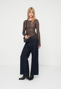 Top de encaje negro de manga larga con patrón texturizado, combinado con jeans oscuros de tiro alto y pierna ancha, y botas de tobillo negras con tacón ancho.