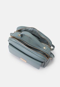 En blå læder crossbody taske med flere lynlåslommer, hardware i guldfarve og en struktureret finish. Nøglefunktionen inkluderer en logo-plade.