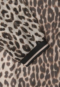 Vêtement à manches longues avec un motif léopard beige et marron, doté d'un poignet noir avec une bande blanche au niveau du poignet.