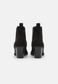 Musta mokkanahka nilkkurit, joissa on teksturoitu pinta, lyhyt lohkakorko ja vetonauhat. Sivujen elastiset paneelit parantavat käyttömukavuutta.