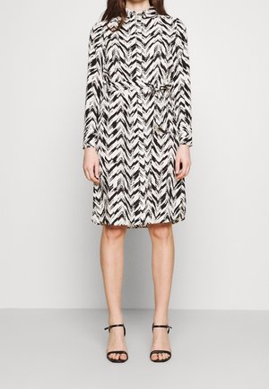 Schwarz-weißes Kleid mit Zickzackmuster, langen Ärmeln, einem taillierten Gürtel und einer Knopfleiste. Trägt man mit schwarzen Riemchensandalen.