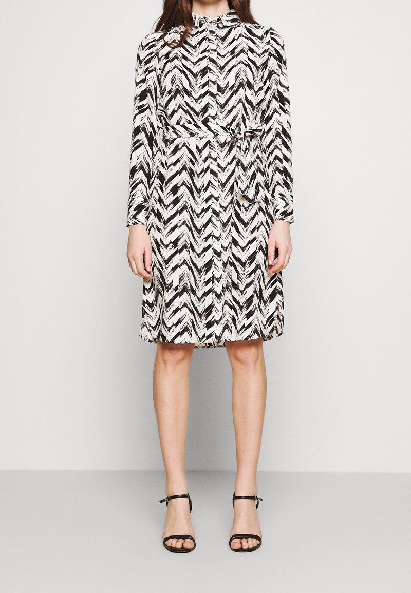 Black and white chevron-patterned dress with long sleeves, a belted waist, and a button-up front. Worn with black strappy sandals.